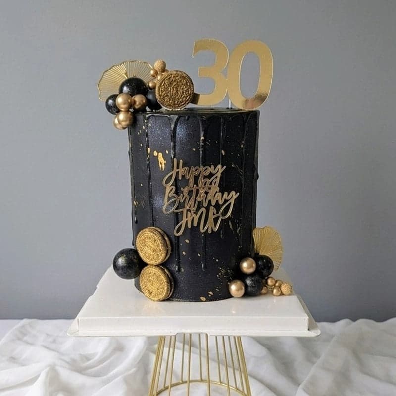 A black and gold celebration cake finished with a gold acrylic topper