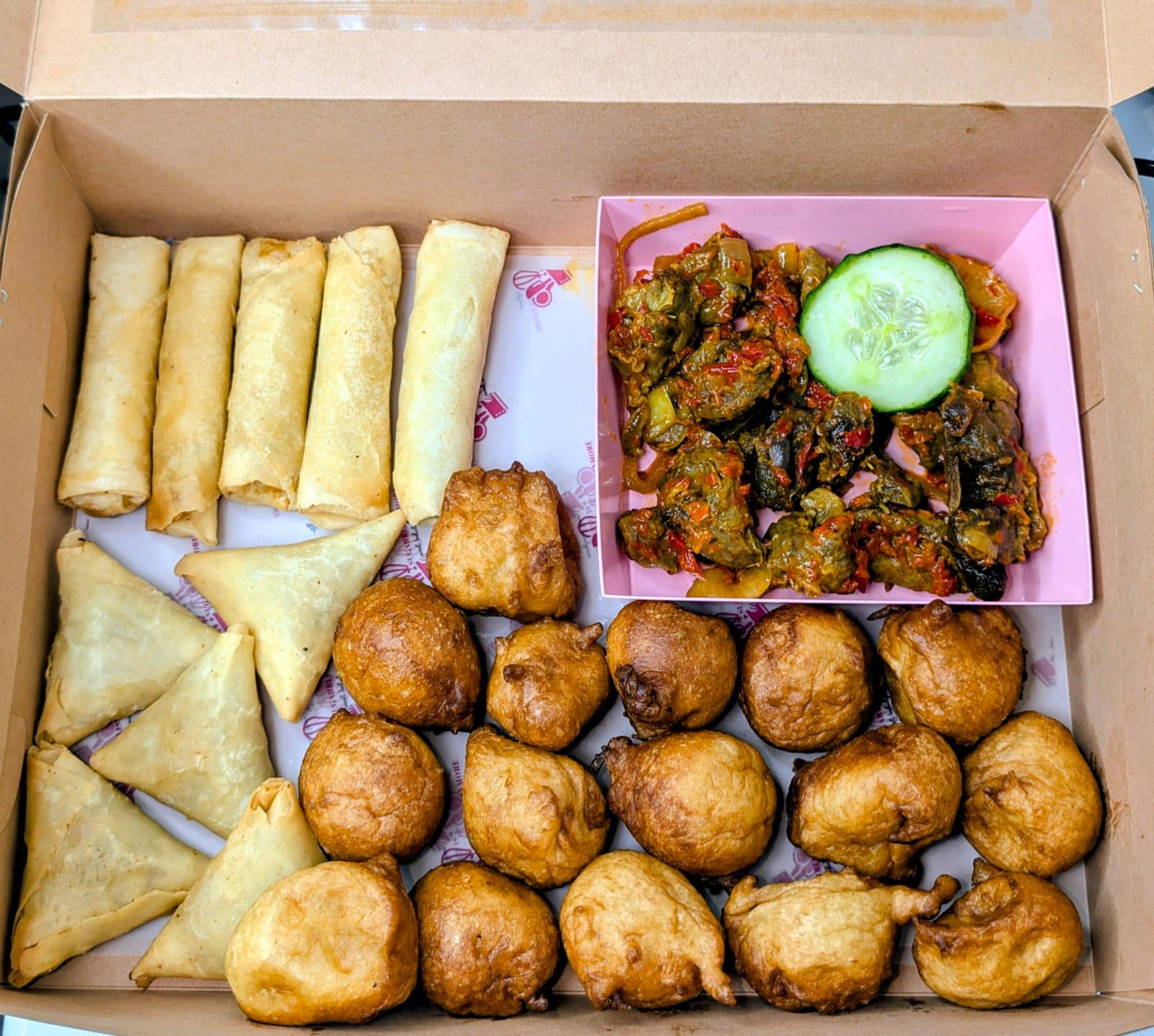 A box of small chops with spring rolls, samosas, puff puff and peppered gizzard