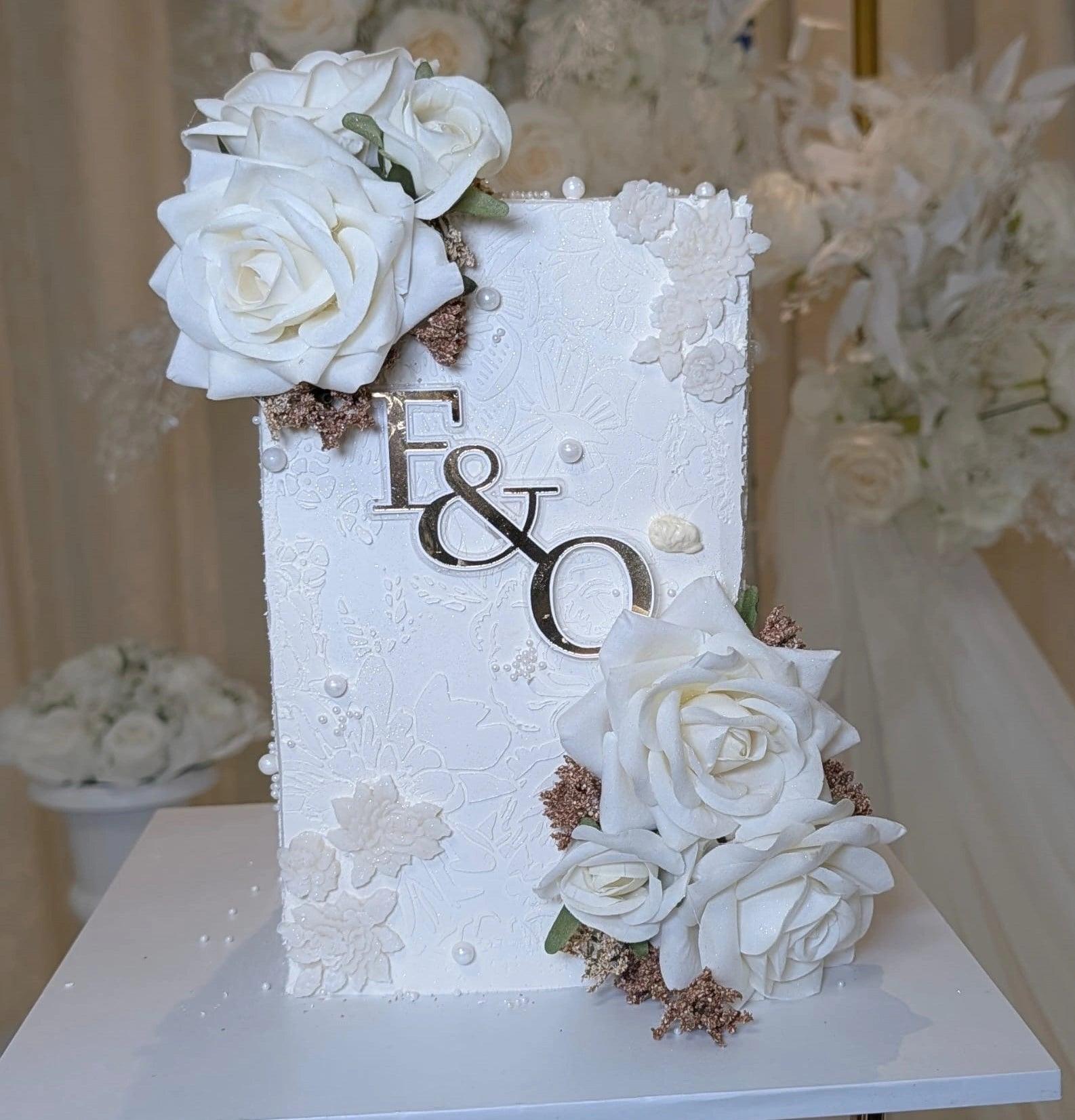 A white square wedding cake with stencilled lace and sugar blossoms